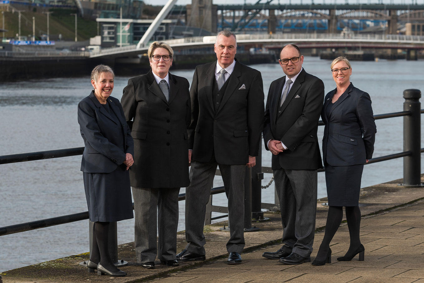 The team from WS Harrison funeral directors in Benton stand together on a bridge wearing smart uniforms